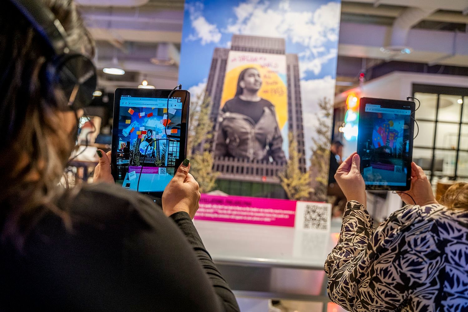 Two users holding tablets up to a large poster. The tablets' screens show an augmented reality experience.