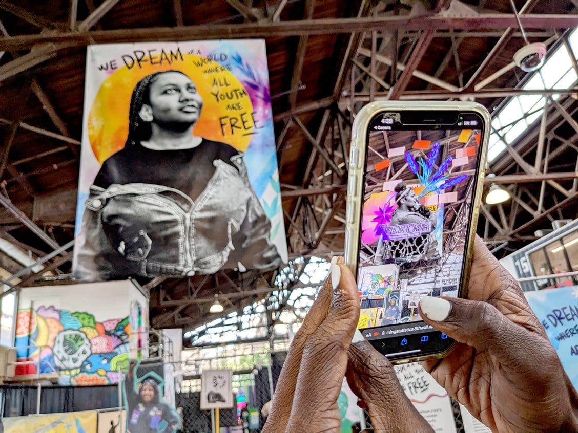 A phone being held up to a large banner. The phone's screen shows an augmented reality experience.