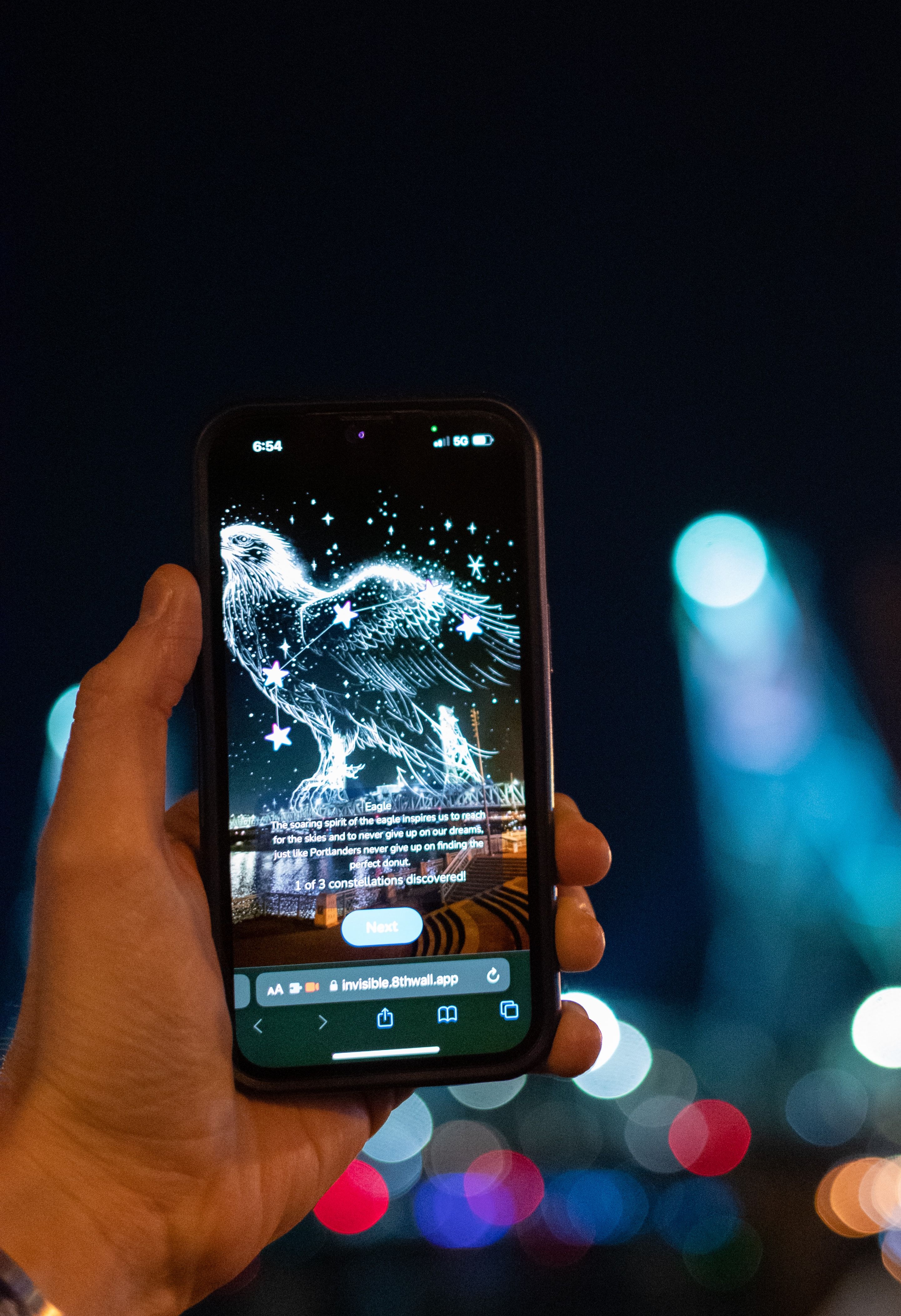 A hand holding a mobile phone. On screen is a constellation forming an Eagle.
