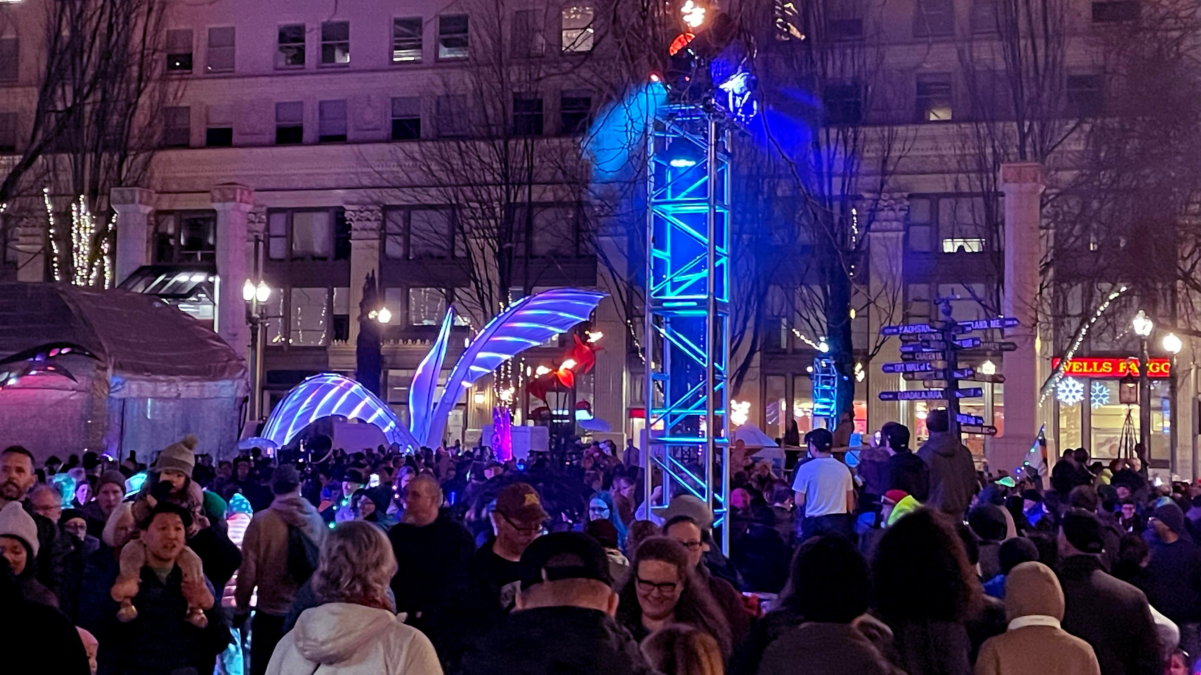 An illuminated art sculpture surrounded by a crowd.