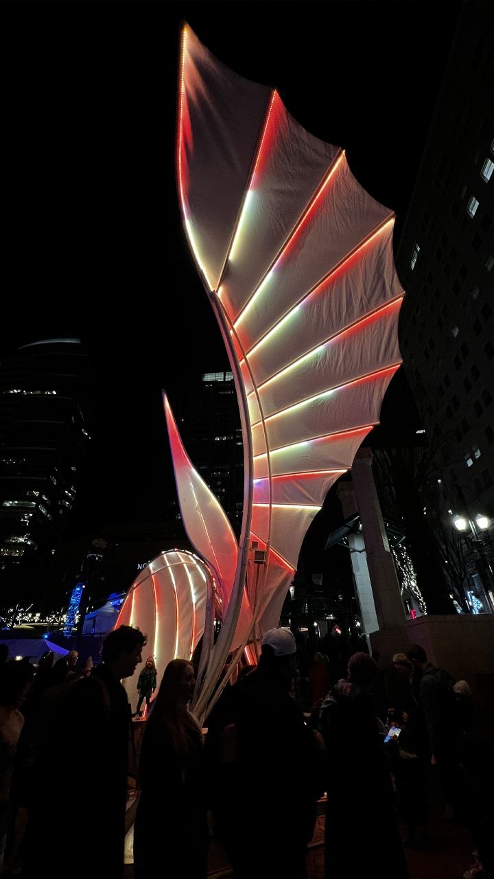 An illuminated art sculpture surrounded by a crowd.