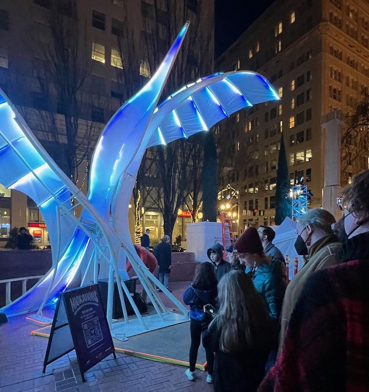 An illuminated art sculpture surrounded by a crowd.